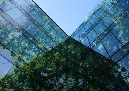Gläserne Gebäudefront, in der sich Bäume spiegeln.