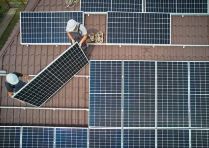 Vogelperspektive auf zwei Arbeiter, die eine Photovoltaikanlage auf einem Dach anbringen.