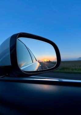 Foto eines Autorückspelegs, aus dem Auto hinaus und bei Dämmerung