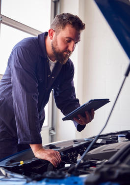 Person mit einem Tablet in der Hand, steht an einer offenen Motorhaube eines Autos