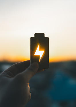 Bild einer Hand die eine Batterie in den Sonnenuntergang hält