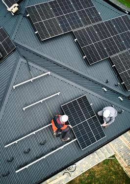 Aus der Vogelperspektive sind zwei Handwerker zu sehen, die ein Solarpanel auf einem Dach befestigen.
