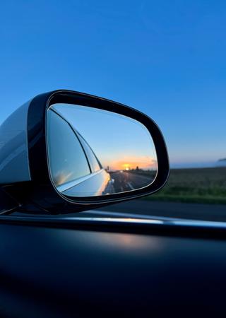 Foto eines Autorückspelegs, aus dem Auto hinaus und bei Dämmerung
