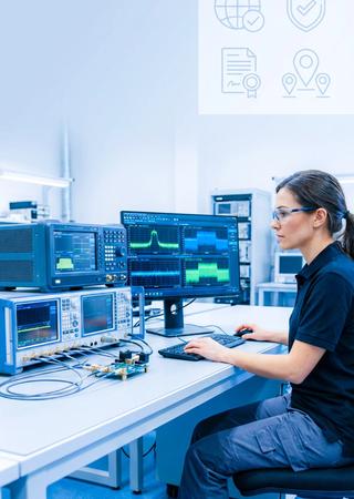 Techniker überwacht Testaufbau, daneben eingeblendete Icons für globale Zertifizierungen.