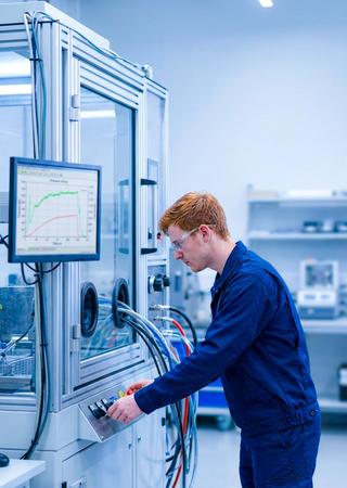 Techniker bedient Prüfkabine, daneben Monitor mit laufender IP-Prüfkurve.