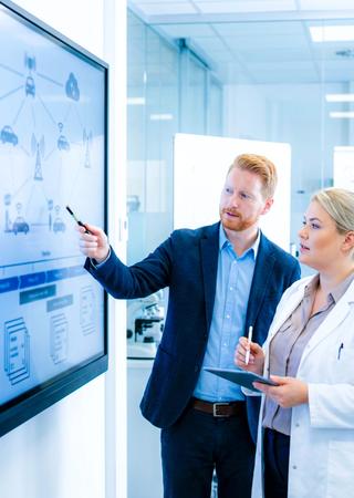 Projektmeeting im Labor, Experten besprechen V2X-Testplan vor großem Display. 