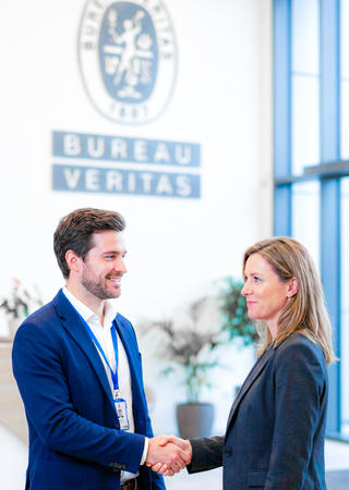 Handschlag zwischen BV‑Mitarbeiter und Kundenvertreter vor Labor- oder Bürohintergrund mit BV‑Branding – Symbol für Partnerschaft und Vertrauen 