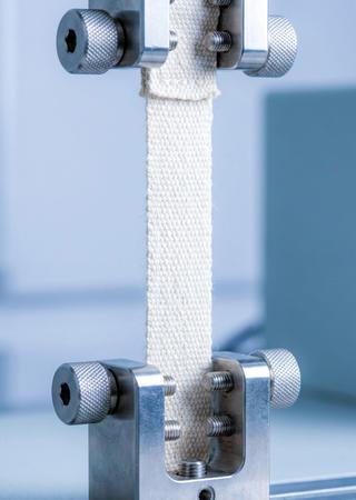 Nahaufnahme eines Stoffmusters, das in einer Zugprüfmaschine oder einem Prüfrahmen eingespannt ist.