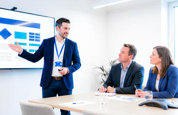 Beratungssituation: BV-Spezialist erklärt Kundenteam Prüfstrategie an großem Bildschirm