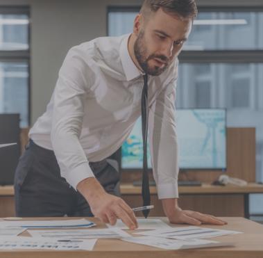 Mann beugt sich über einen Schreibtisch und betrachtet darauf liegende Dokumente.