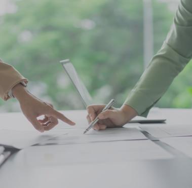 Tisch über den zwei Personen gebeugt sind, deren Arme zu sehen sind. Eine der Person unterzeichnet ein Dokument.