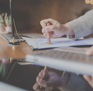 Schreibtisch, an dem eine Person sitzt, die ein darauf liegendes Dokument stempelt.