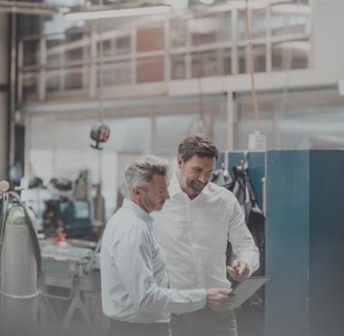 Zwei Männer stehen in einer Produktionshalle und schauen gemeinsam auf ein Dokument.