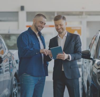 Zwei Männer stehen zwischen zwei Autos und schauen gemeinsam auf ein Tablet.